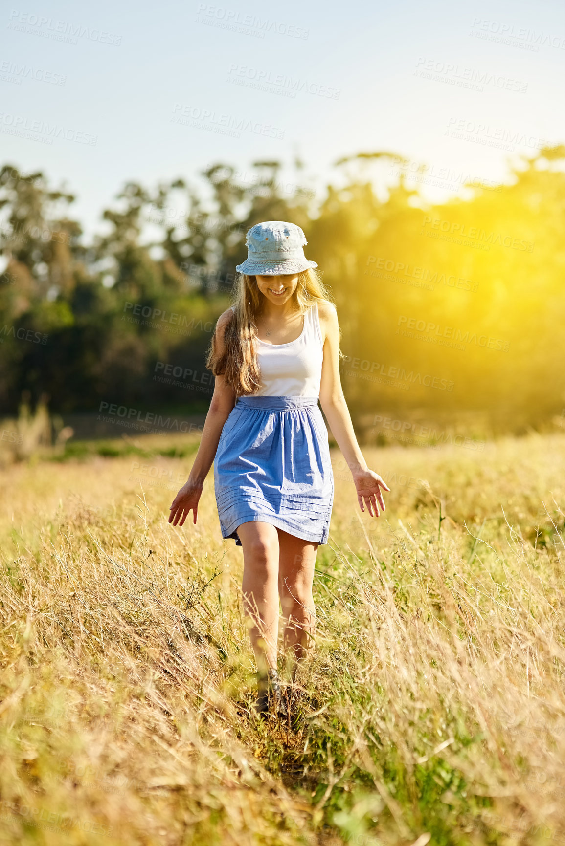 Buy stock photo Woman, walking and happiness in nature for field, travel and adventure in countryside for spring. Gen z, smile and journey in natural environment with flowers, leaves and sun on holiday in France