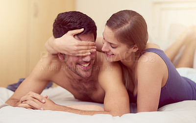 Buy stock photo Shot of a young woman playfully covering her boyfriend's eyes while they lie in bed together