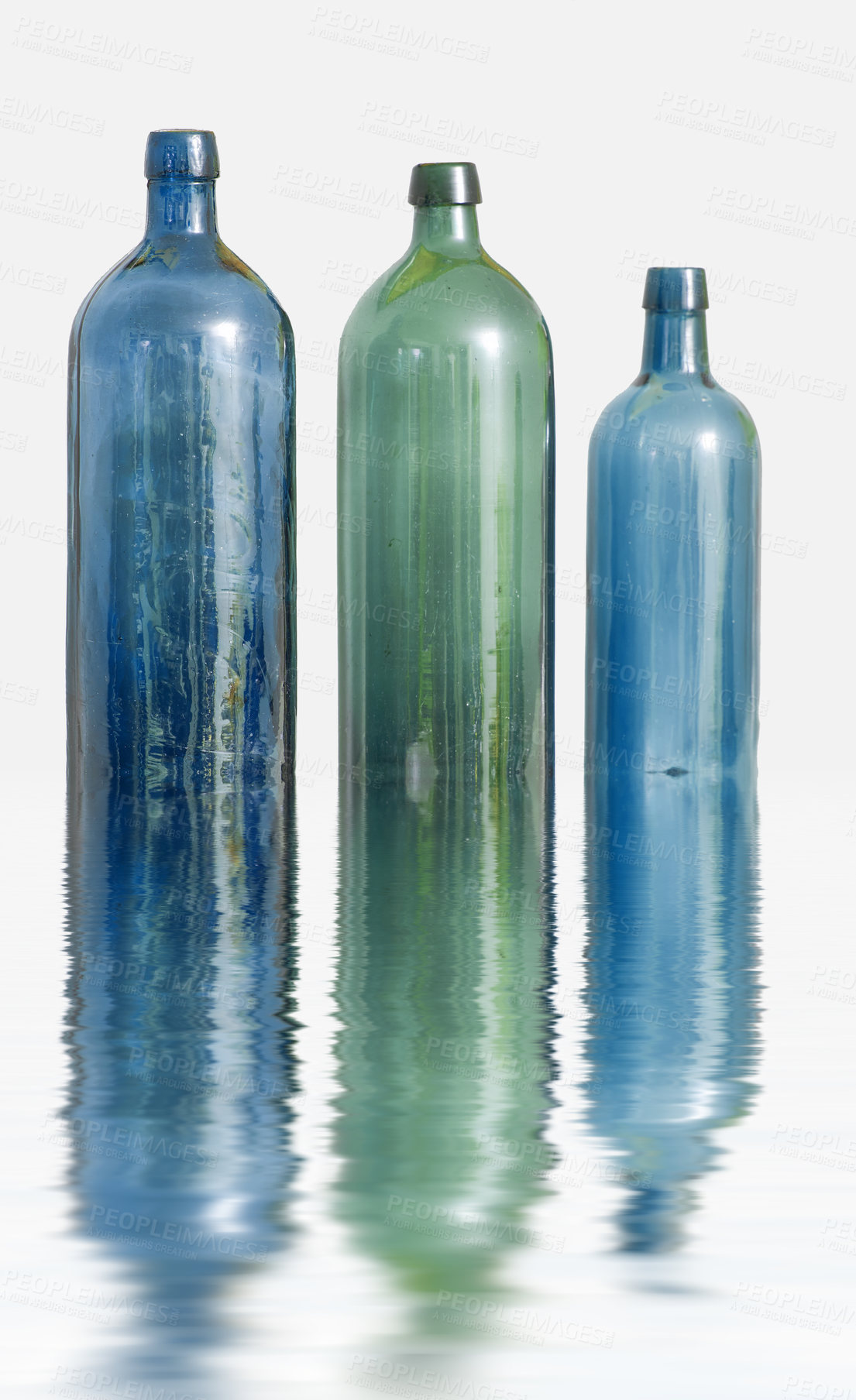 Buy stock photo Three glass bottles on white surface with water effect. Old colorful vintage wine bottles arranged against a copy space background with reflections. Side view of unused containers in descending order