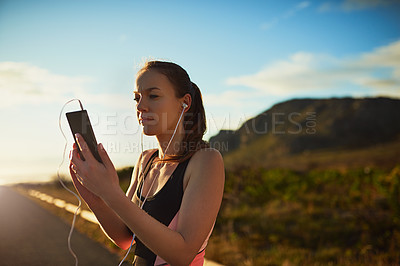 Buy stock photo Shot of a sporty young woman organizing her workout playlist outdoors