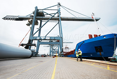 Buy stock photo An anchored ship on the dock with cargo being loaded on to it with cranes and two people standing next to the ship