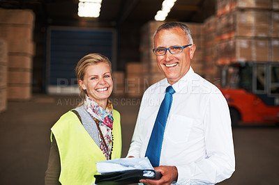 Buy stock photo Two happy colleagues standing in a warehouse and going over plans.