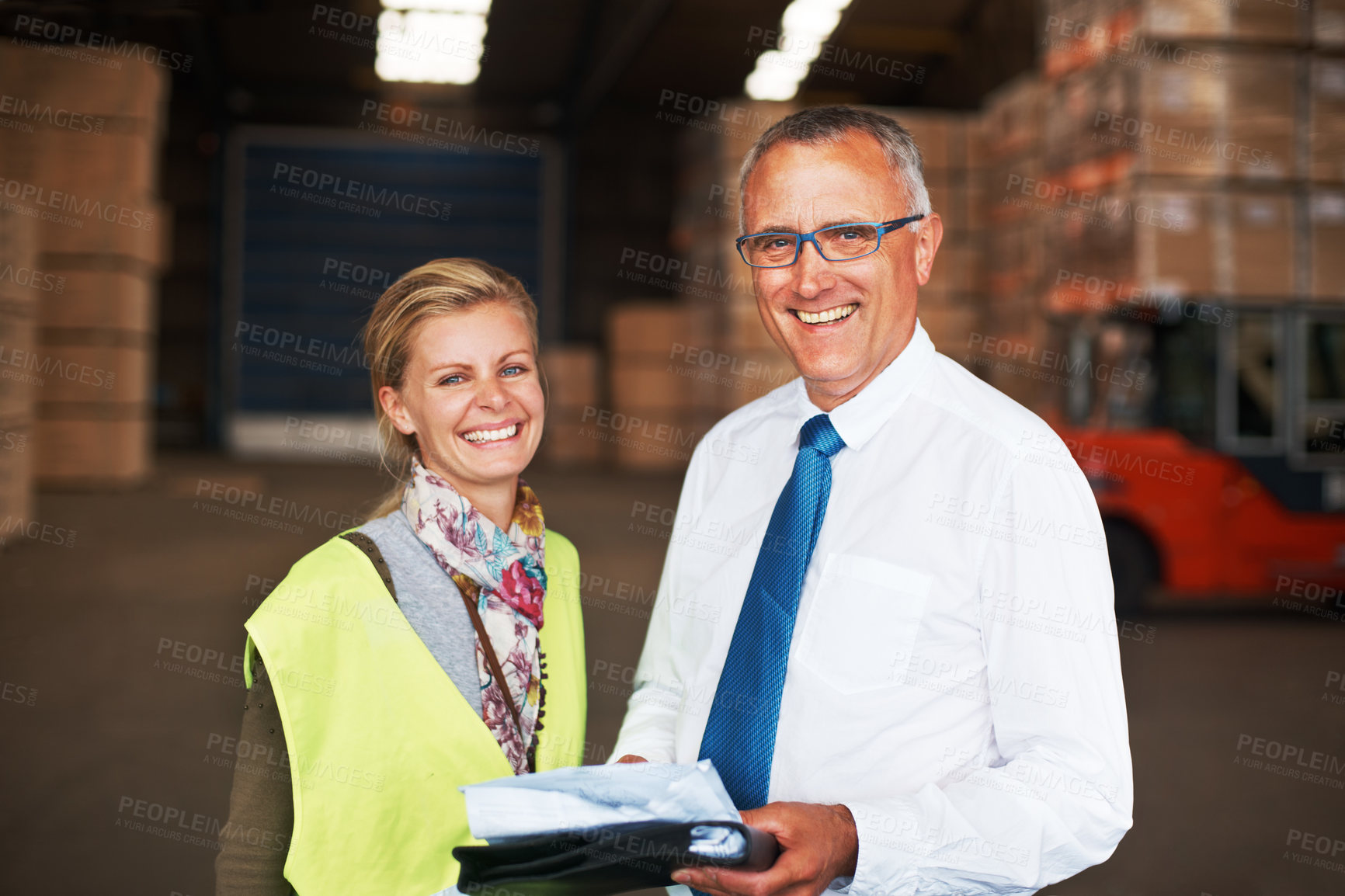 Buy stock photo Two happy colleagues standing in a warehouse and going over plans.