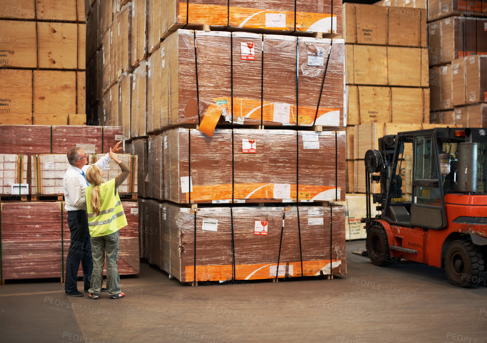 Buy stock photo Two colleagues standing in a warehouse and pointing up to the goods close to a fork lift.