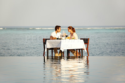 Buy stock photo Romantic, happy and a couple at the beach for dinner in the ocean, conversation and a date. Smile, love and a man and woman with lunch, breakfast or eating in the water of the sea on a holiday
