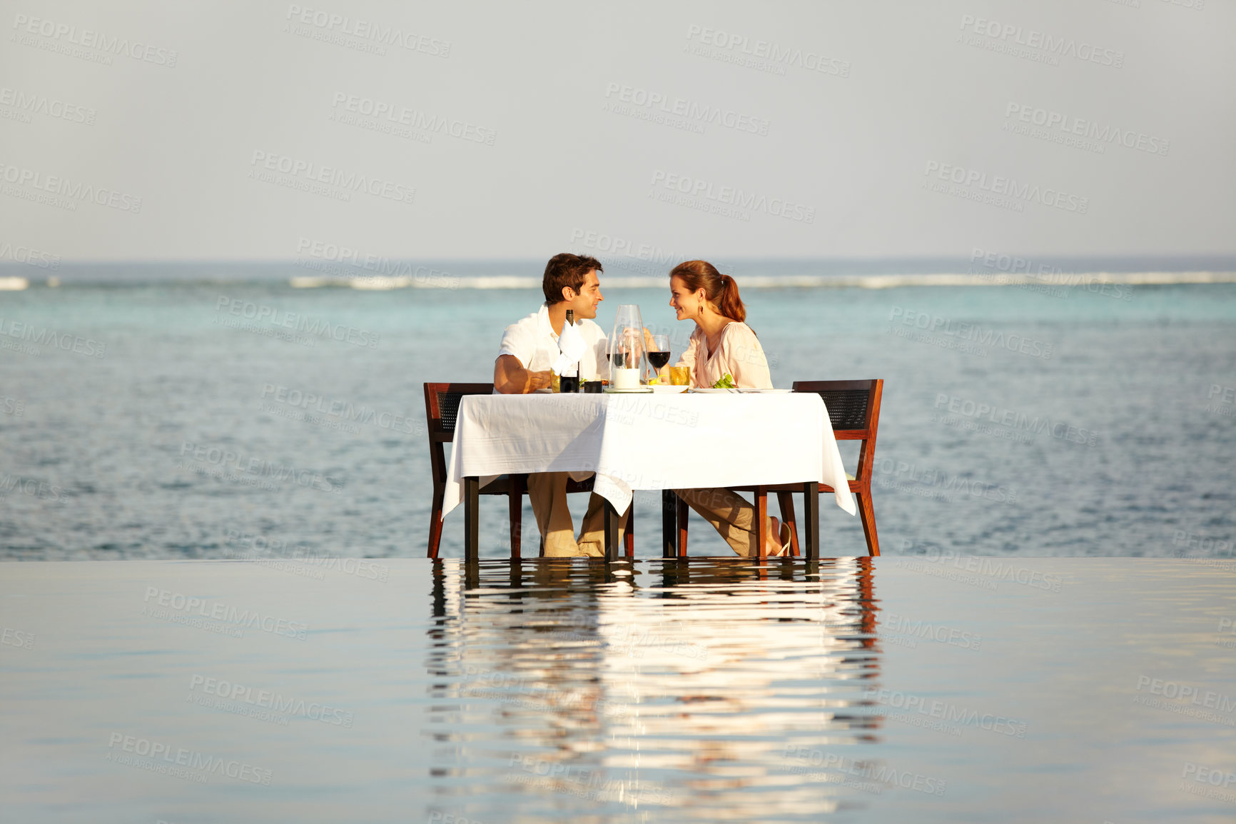 Buy stock photo Romantic, happy and a couple at the beach for dinner in the ocean, conversation and a date. Smile, love and a man and woman with lunch, breakfast or eating in the water of the sea on a holiday