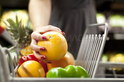 Buy stock photo A woman&#039;s hand placing an orange into a shopping cart