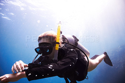 Buy stock photo Young female scuba diver floating through the water as she checks her dive computer - Copyspace