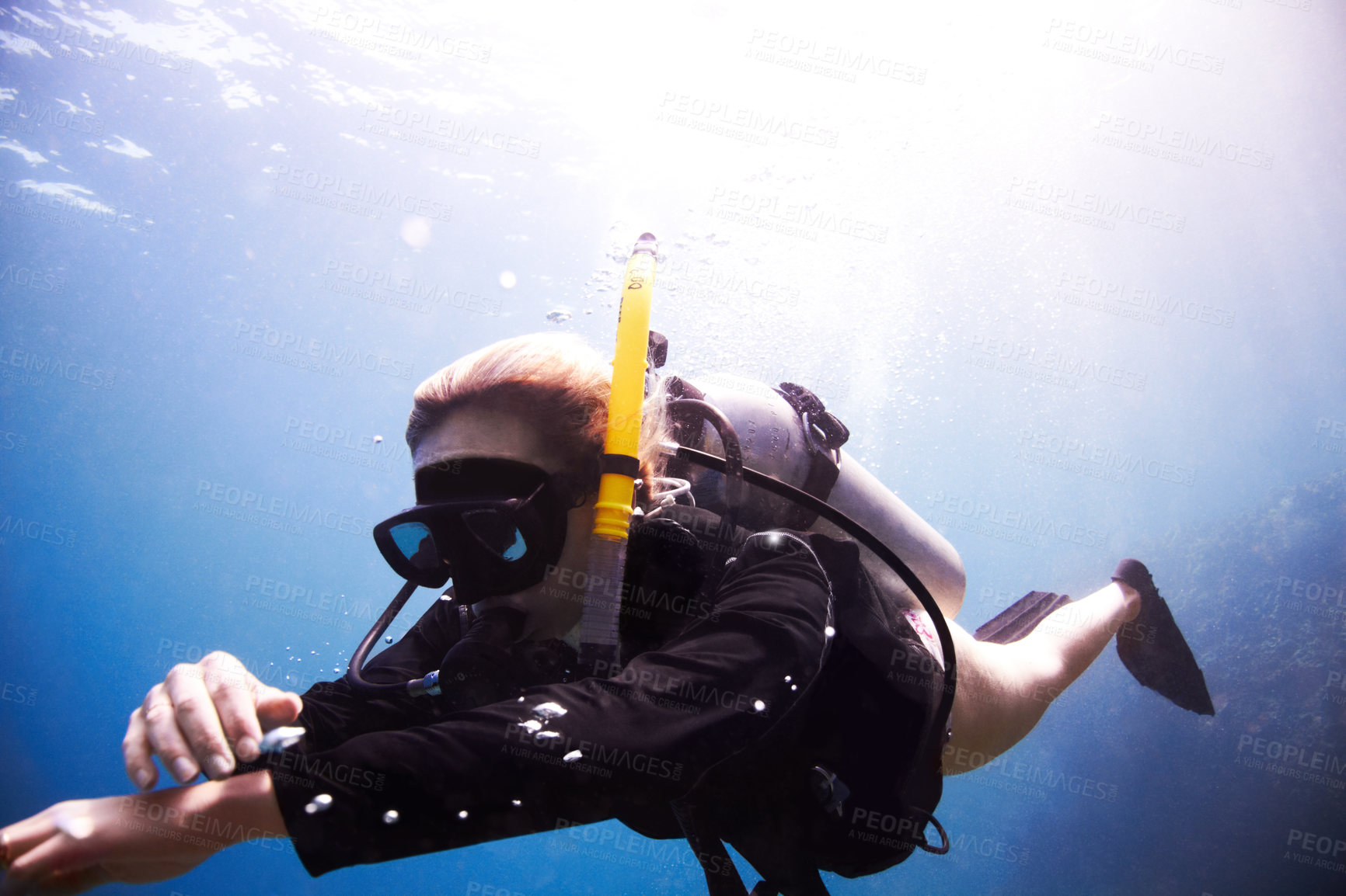 Buy stock photo Young female scuba diver floating through the water as she checks her dive computer - Copyspace