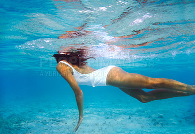 Buy stock photo Underwater shot of a beautiful young woman swimming in blue ocean