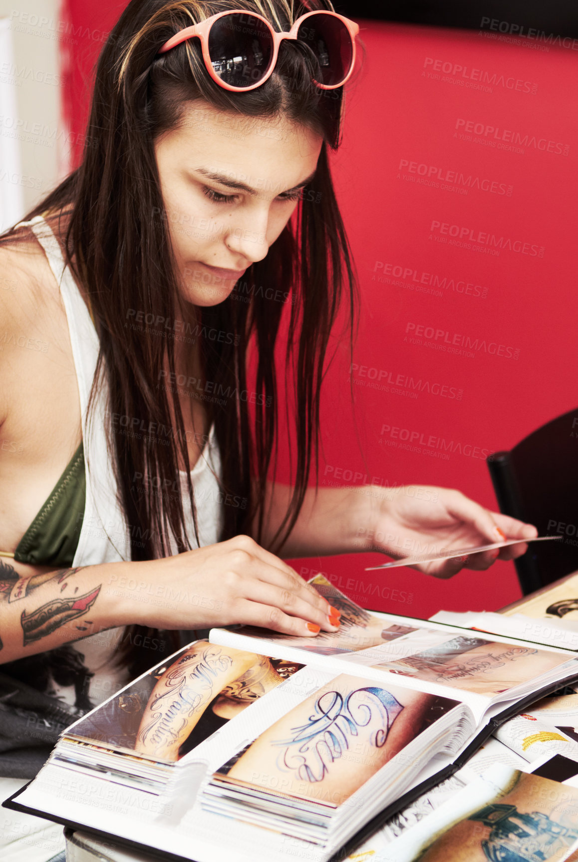 Buy stock photo Shot of a beautiful young tattooed woman paging through an album of tattoo designs