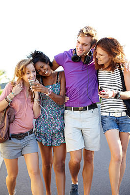 Buy stock photo Four friends sharing their music while walking down the street