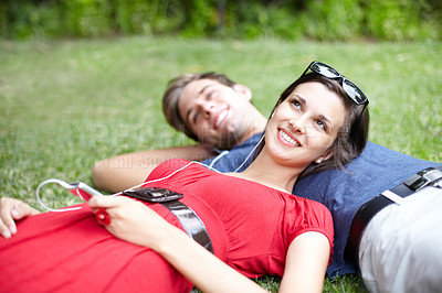 Buy stock photo Young couple lying in a park on the grass while the woman listens to music