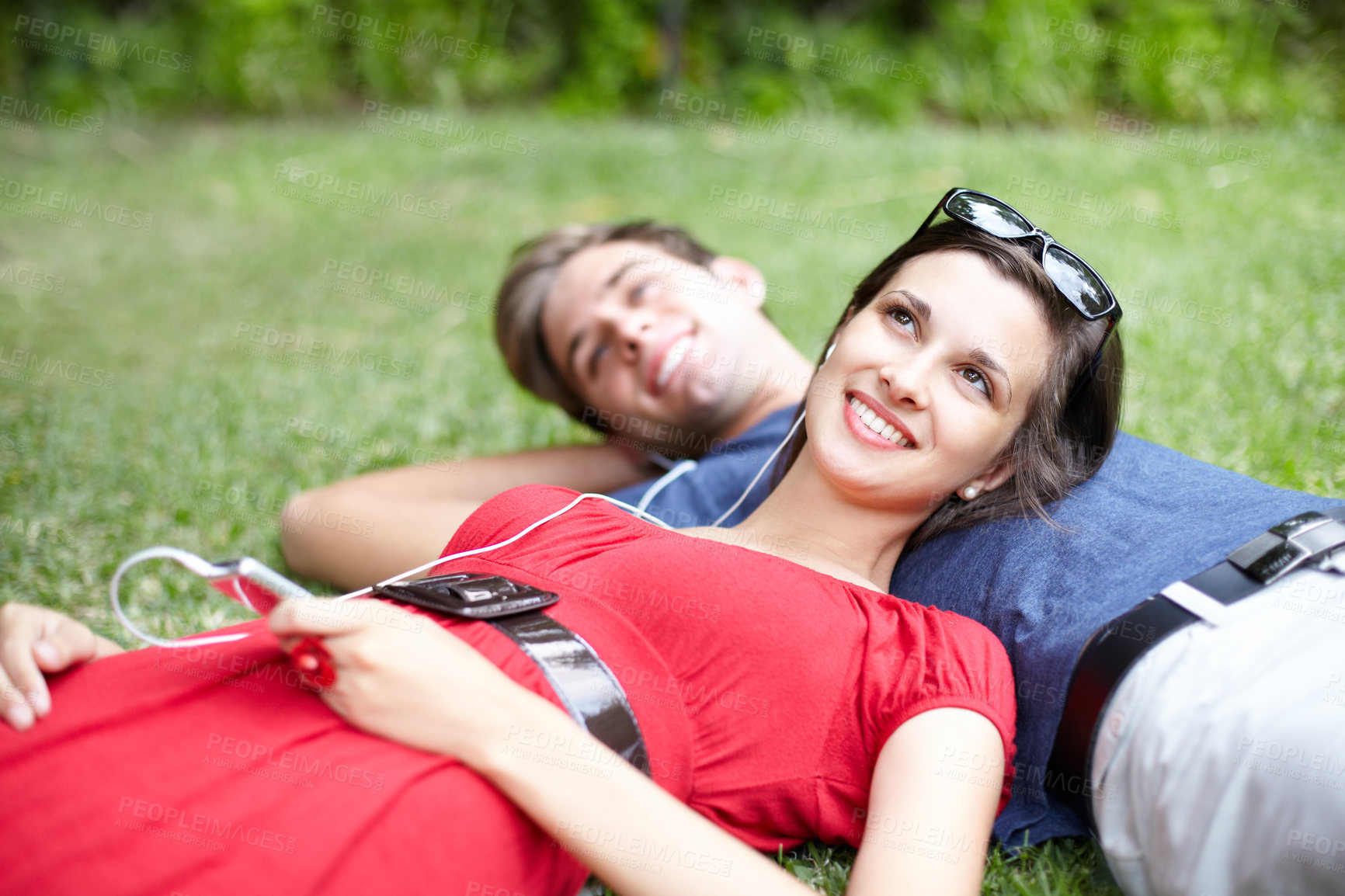 Buy stock photo Young couple lying in a park on the grass while the woman listens to music