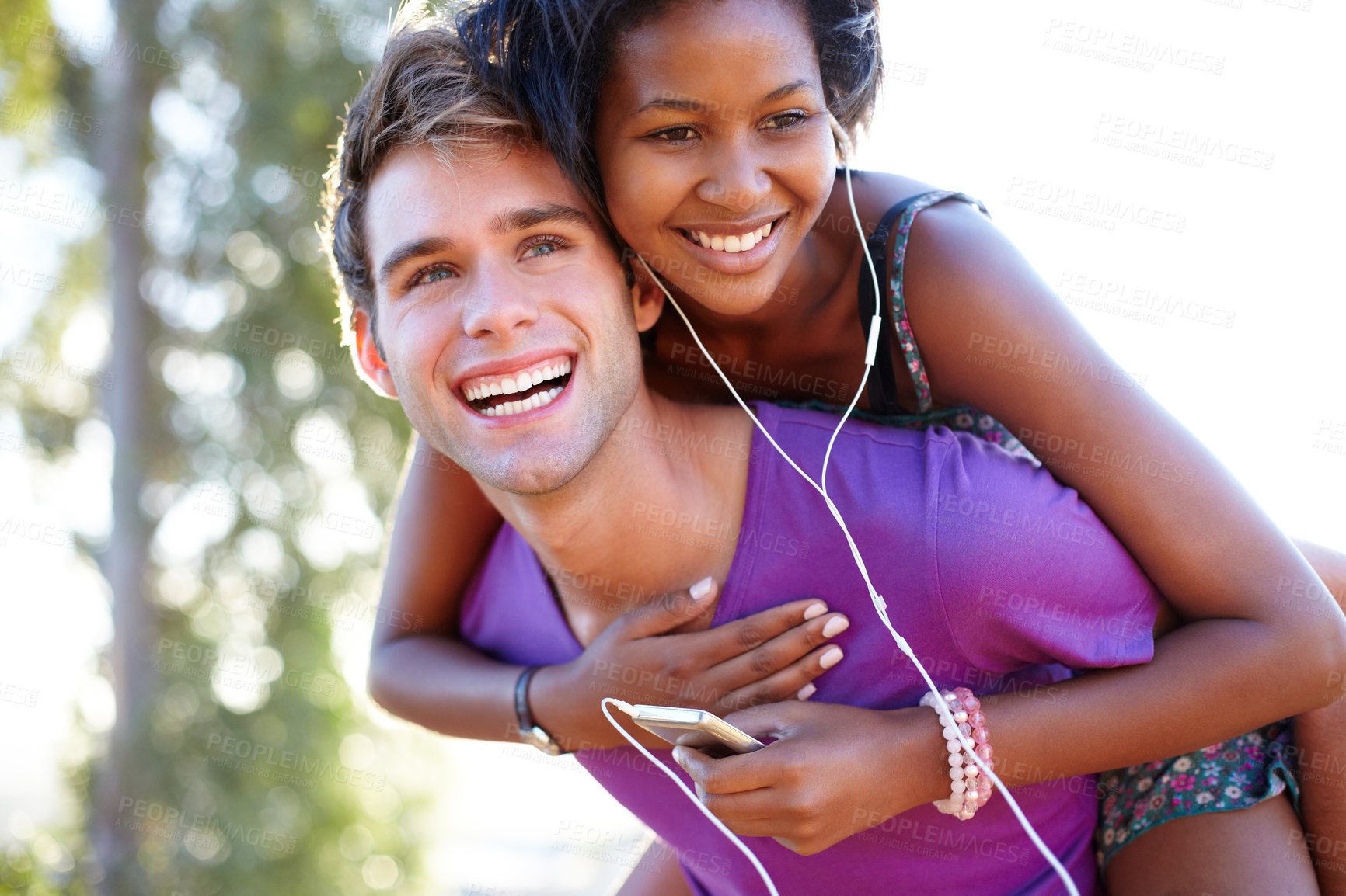 Buy stock photo Fitness, smile and happy couple with piggyback hug in a park for training, bond or fun. Interracial, love and face of active man with back ride for woman with music, earphones or audio mp3 player