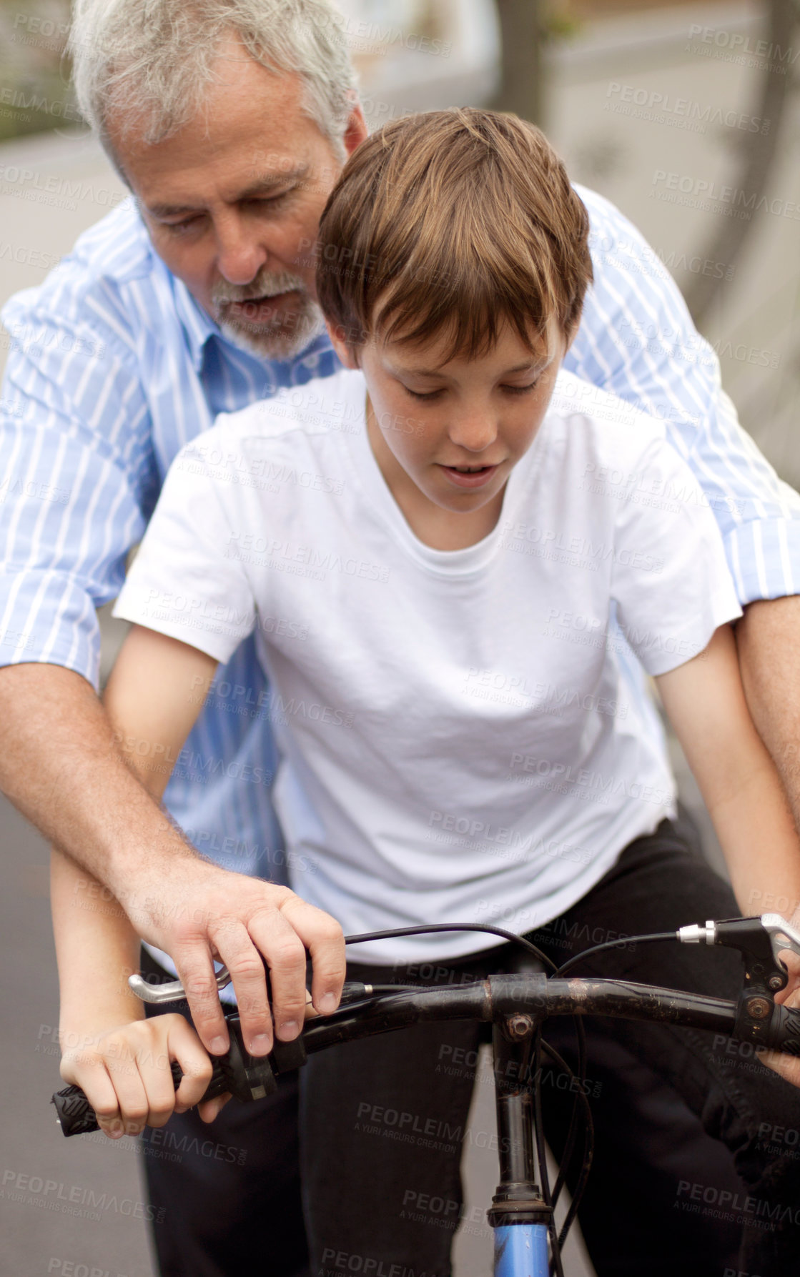 Buy stock photo Young boy learning how to ride a bicycle with his father's help