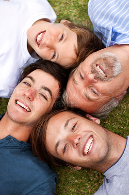 Buy stock photo Father and sons lying down on the grass with their heads beside one another