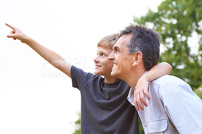 Buy stock photo Young boy hold his arm around his father's neck while pointing up into the sky