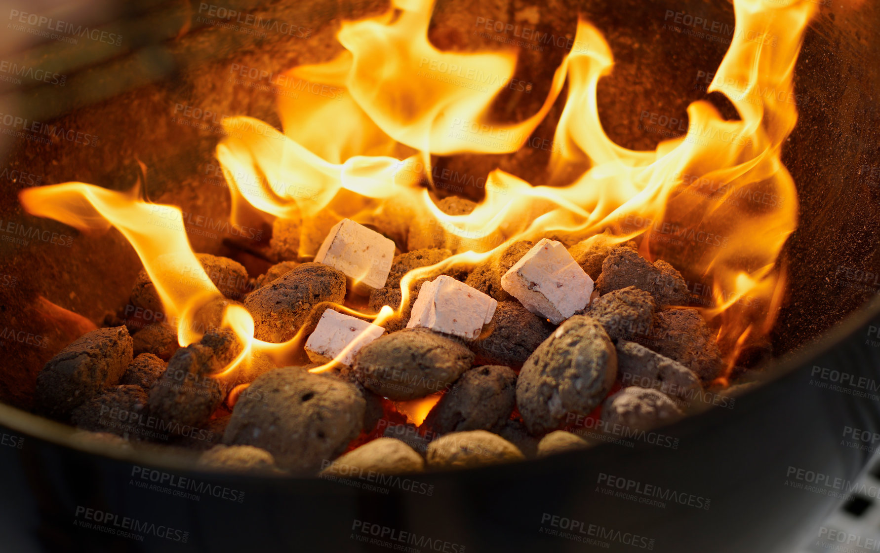 Buy stock photo Getting ready to bbq on weekend. Closeup of a warm fire burning in a barbeque at night. Zoomed in on texture and detail on charcoal bricks and fire starters in a metal fire pit outside in the evening