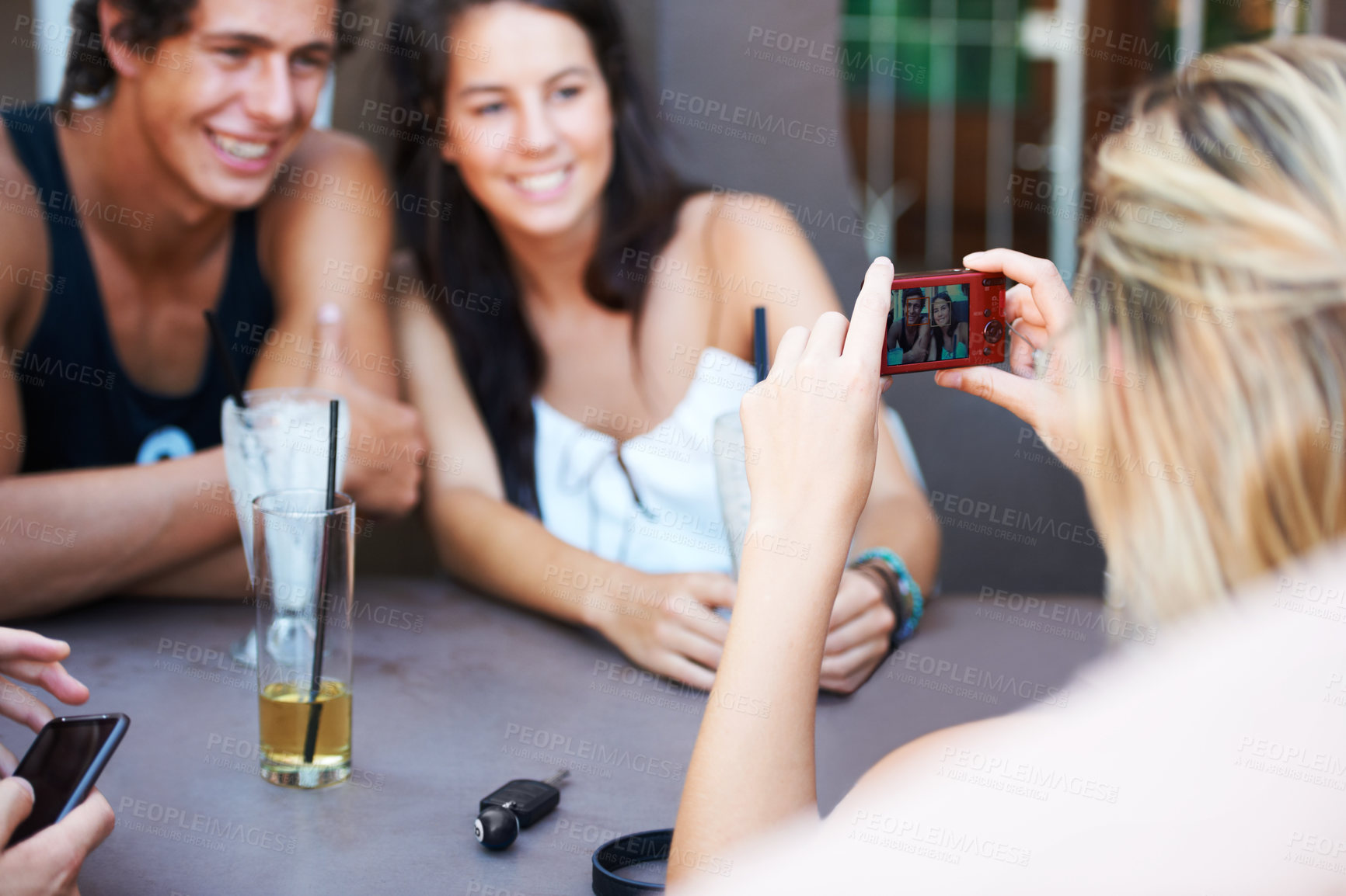 Buy stock photo Group of teens enjoying beverages while at an outdoor restaurant while taking a photo with a mobile phone