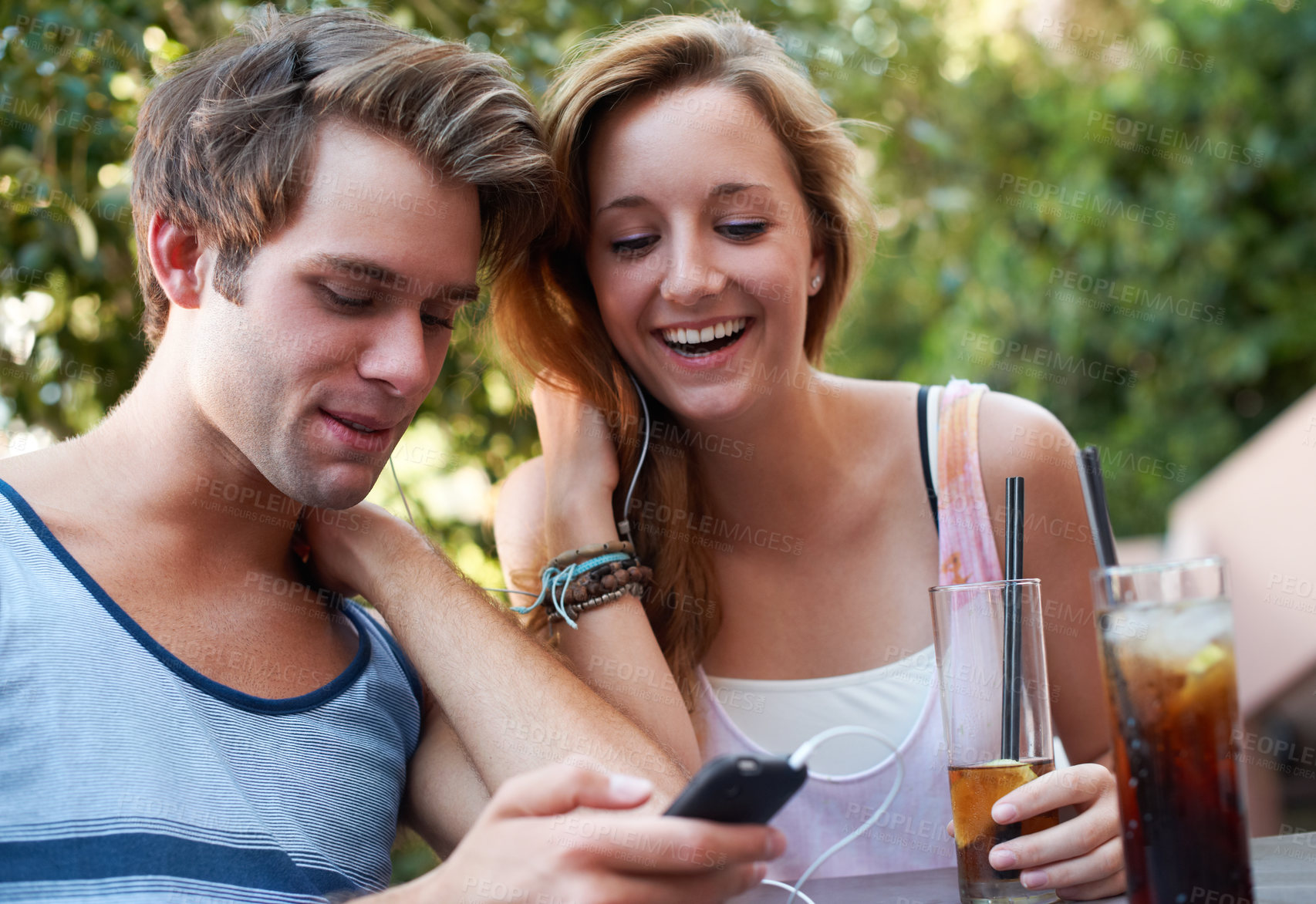 Buy stock photo Cute teen couple sharing an MP3 player and listening to music while enjoying their beverages
