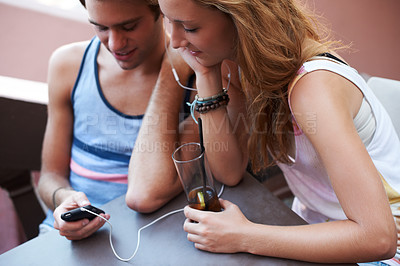 Buy stock photo Happy teen couple sharing an MP3 player and listening to music while enjoying their beverages