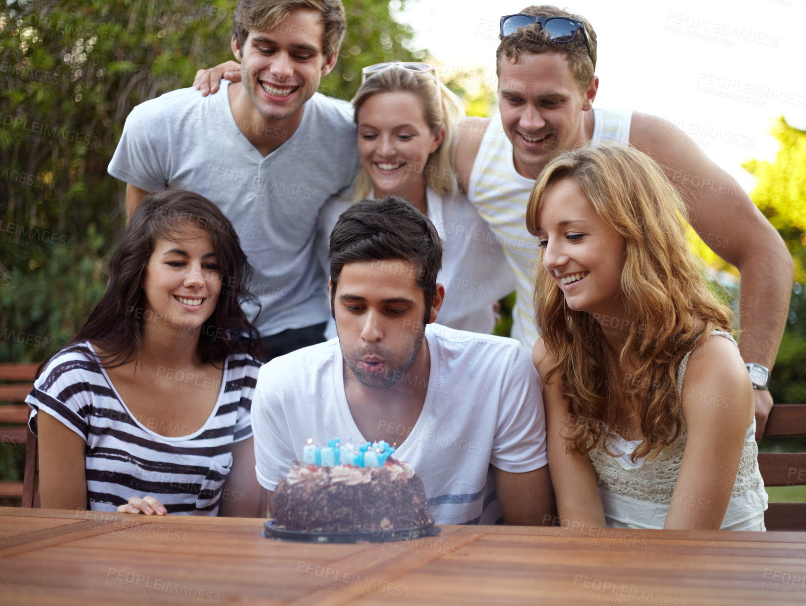 Buy stock photo Birthday, people and blow candles outdoor for celebration, surprise or party with milestone or happiness. Cake, men and women in backyard of home or nature with gathering or social event with smile