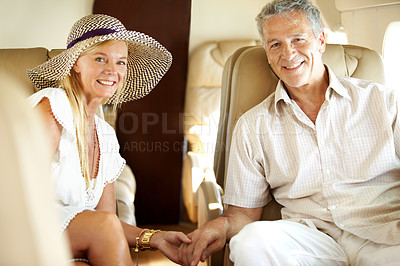 Buy stock photo Smiling senior couple holding hands on an airplane heading overseas - portrait