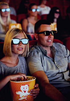 Buy stock photo Couple watch a movie together in a cinema with 3D glasses while eating popcorn or a snack. Young man and woman sitting watching an action movies or film for entertainment during a date in a theatre
