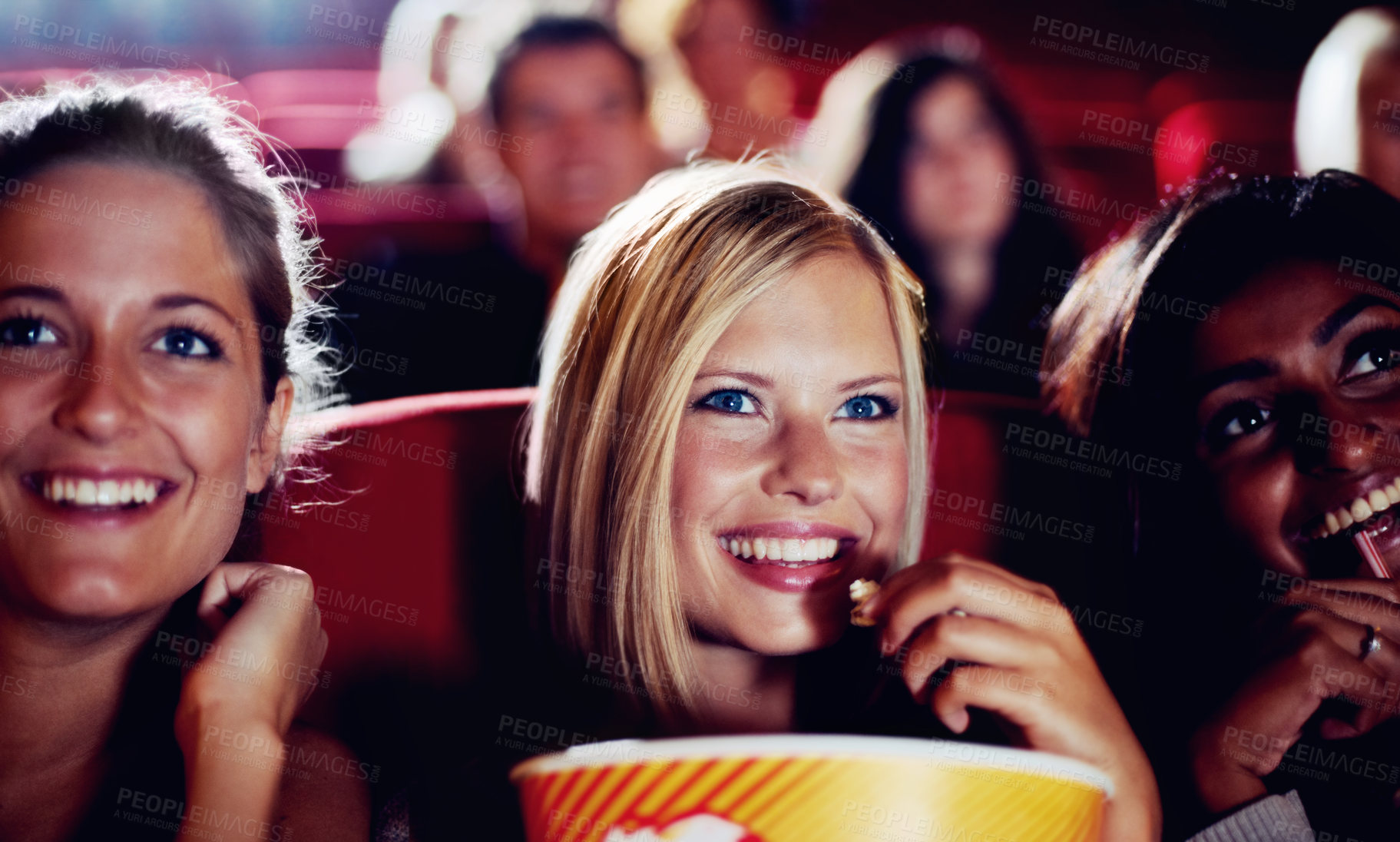 Buy stock photo Three friends laughing during a movie while eating popcorn