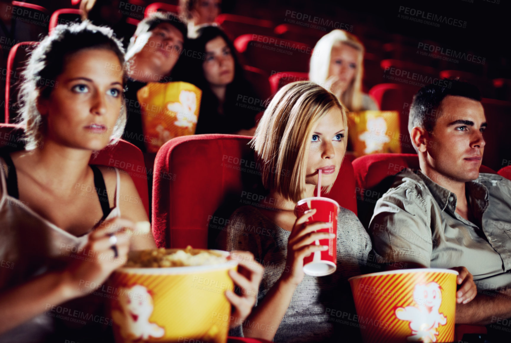 Buy stock photo Friends sitting with refreshments and popcorn enjoying a movie together