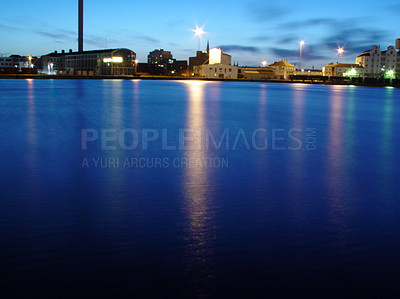 Buy stock photo Ocean, night and buildings in port with lights, reflection on calm blue water or holiday location. City at sea in evening, travel, skyline and nature, urban beach village for vacation, peace and view