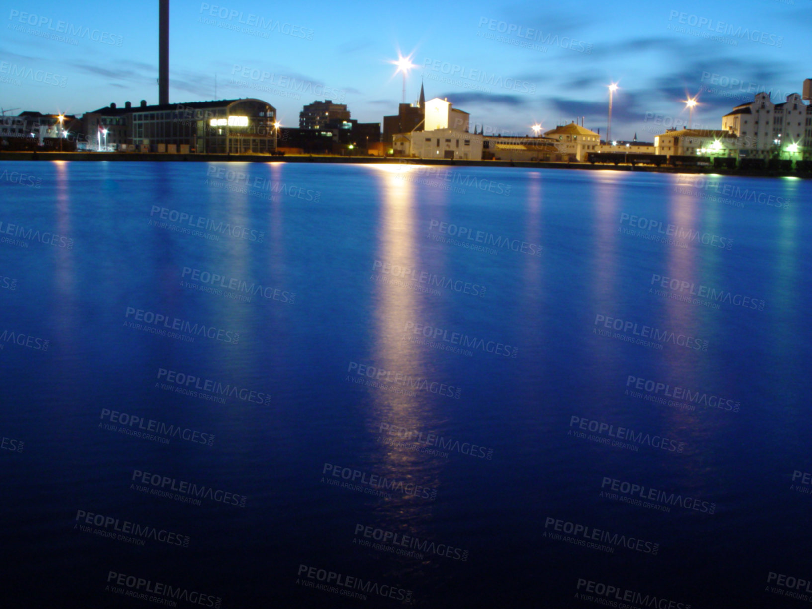 Buy stock photo Ocean, night and buildings in port with lights, reflection on calm blue water or holiday location. City at sea in evening, travel, skyline and nature, urban beach village for vacation, peace and view