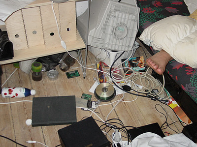 Buy stock photo Closeup of a messy bedroom with a foot sticking out from under dirty bed covers. Untidy teenager room with tangled wire, electronics, equipment and clutter lying on the floor next to an unmade bed