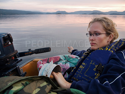 Buy stock photo A real-life image of a beautiful young woman relaxing in a boat on a lake at sunset