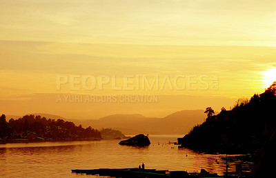 Buy stock photo Silhouette figures of two people enjoying the view. Beauty in nature on a calm lake during a summer evening. A panoramic of a lake with small islands during an orange sunset at twilight