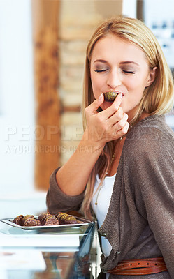 Buy stock photo Pretty young woman biting in to a sample chocolate at the shops