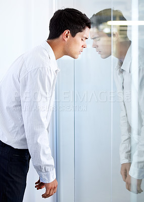 Buy stock photo A young businessman hitting his head against a glass door with a look of defeat on his face