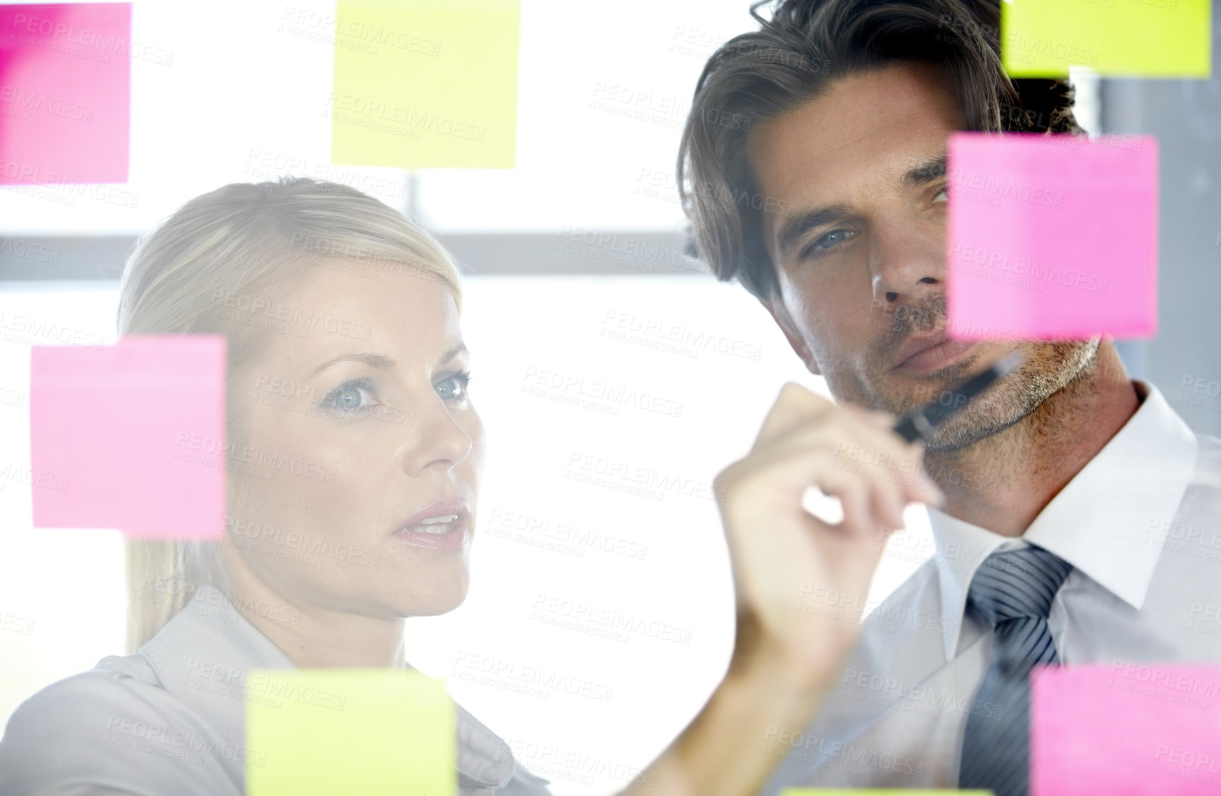 Buy stock photo A man and woman in the office looking at notes on a glass window, discussing and deciding