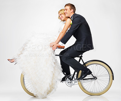 Buy stock photo Happy, wedding and couple on a bicycle against a white background, after getting married together. Love, young bride and groom in dress and suit, cycling on a bike in marriage happiness or bliss 