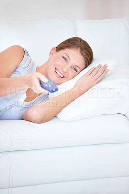 Buy stock photo Smiling young woman relaxing at home on the couch using her TV remote - portrait