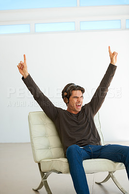 Buy stock photo Happy, headphones and young man on a chair listening to music, playlist or radio at home. Excited, scream and male person streaming a song or album for singing karaoke in modern apartment or house.