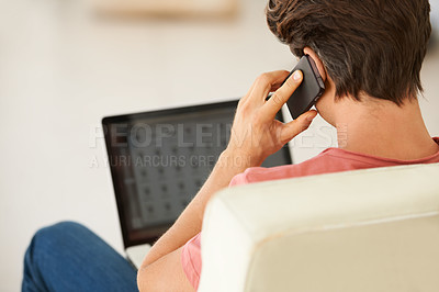 Buy stock photo Rear-view of a young man talking on his mobile while using his laptop