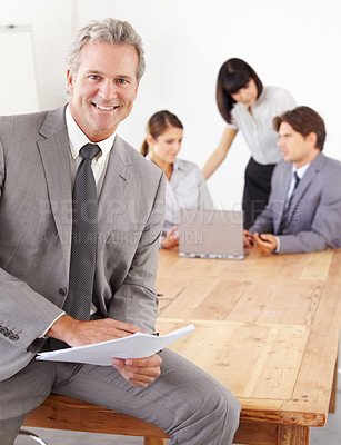 Buy stock photo A goodlooking senior business manager holding documents while his team sits in the background