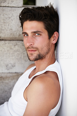 Buy stock photo Handsome young male staring at you while leaning against a wall
