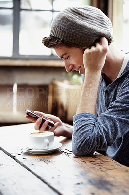 Buy stock photo Shot of young man using a cellphone while sitting in a cafe