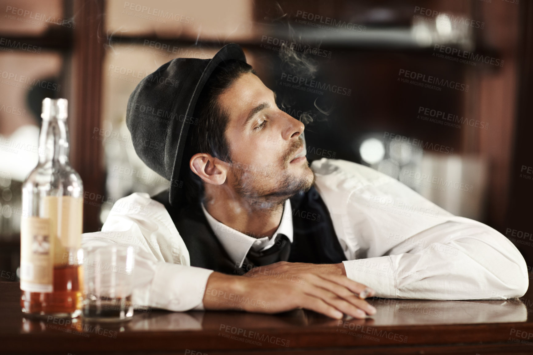 Buy stock photo Whiskey, bar and bartender smoking and drinking in club to relax in waiting for a customer. Alcohol, drink and barman with cigarette, smoke and scotch in glass bottle on table or counter at work