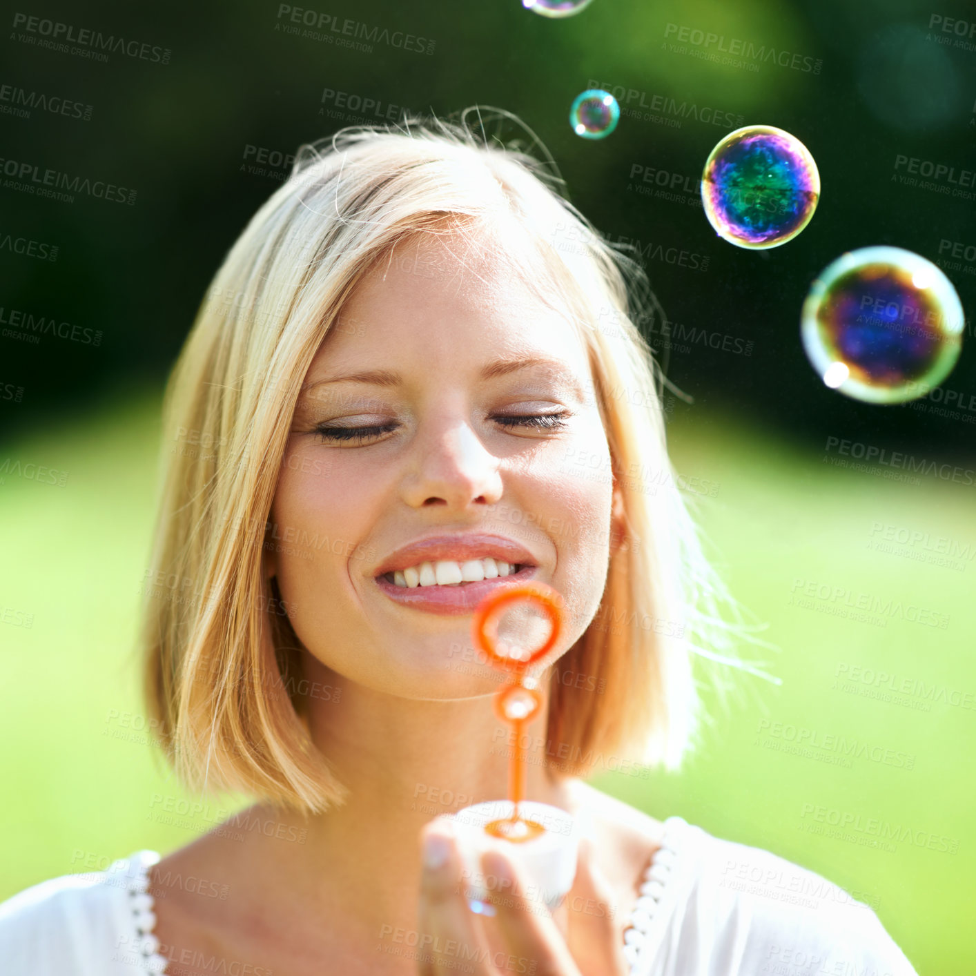 Buy stock photo Happy woman, nature and blowing bubbles with smile for fun day in sunshine at outdoor park. Face of young female person or blonde with stick or wand to blow bubble for playful holiday or summer break