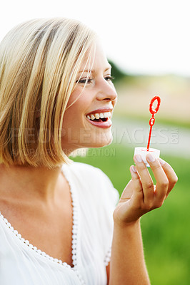 Buy stock photo Happy woman, smile and blowing bubbles in nature for fun day in sunshine at outdoor park. Face of young female person or blonde with stick or wand to blow bubble on playful holiday or summer break