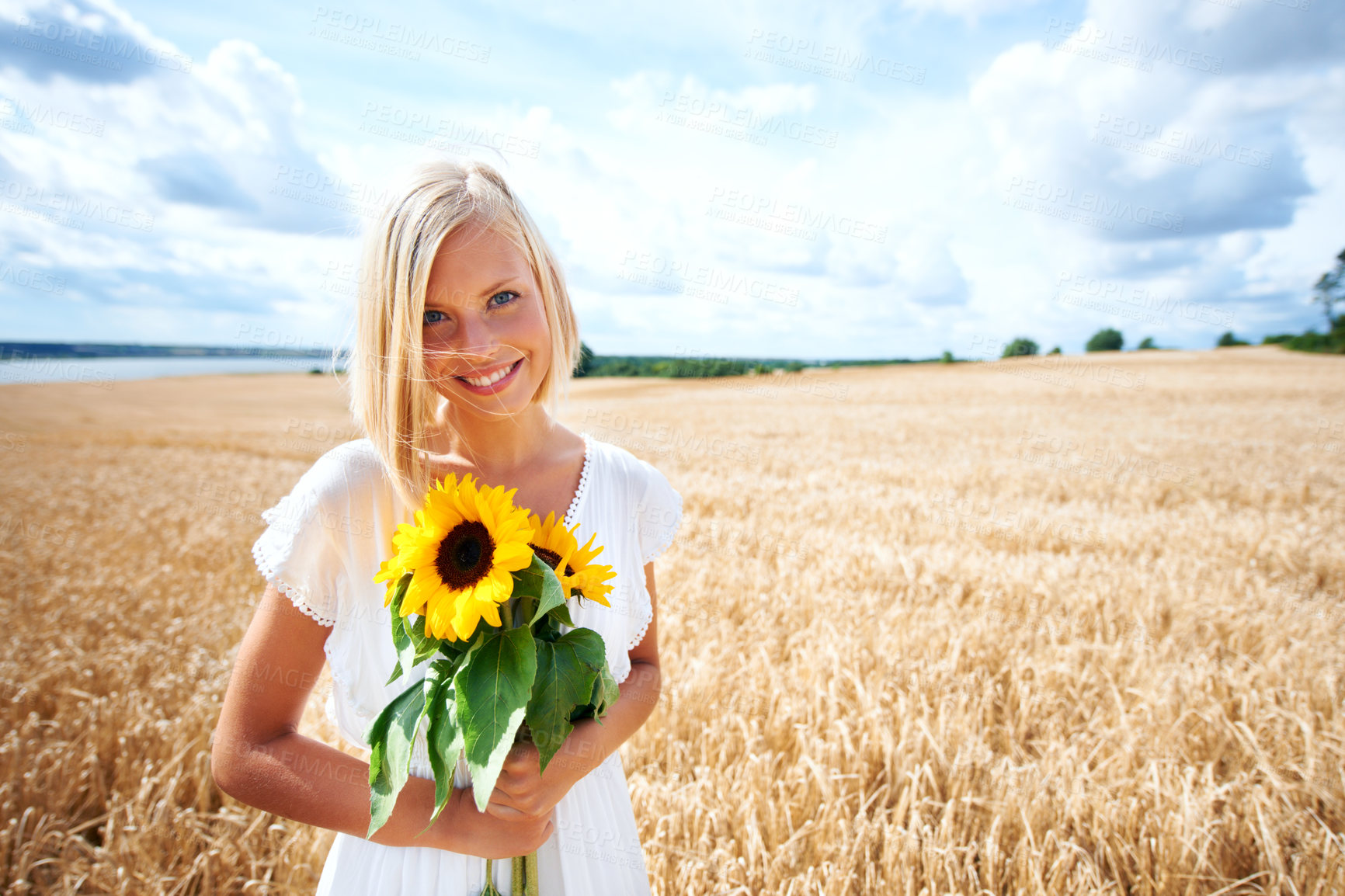 Buy stock photo Happy woman, portrait and flowers in nature countryside on grass or wheat field with cloudy blue sky. Female person or blonde smile with sun flower, plant or blossom in sunshine, travel or vacation 